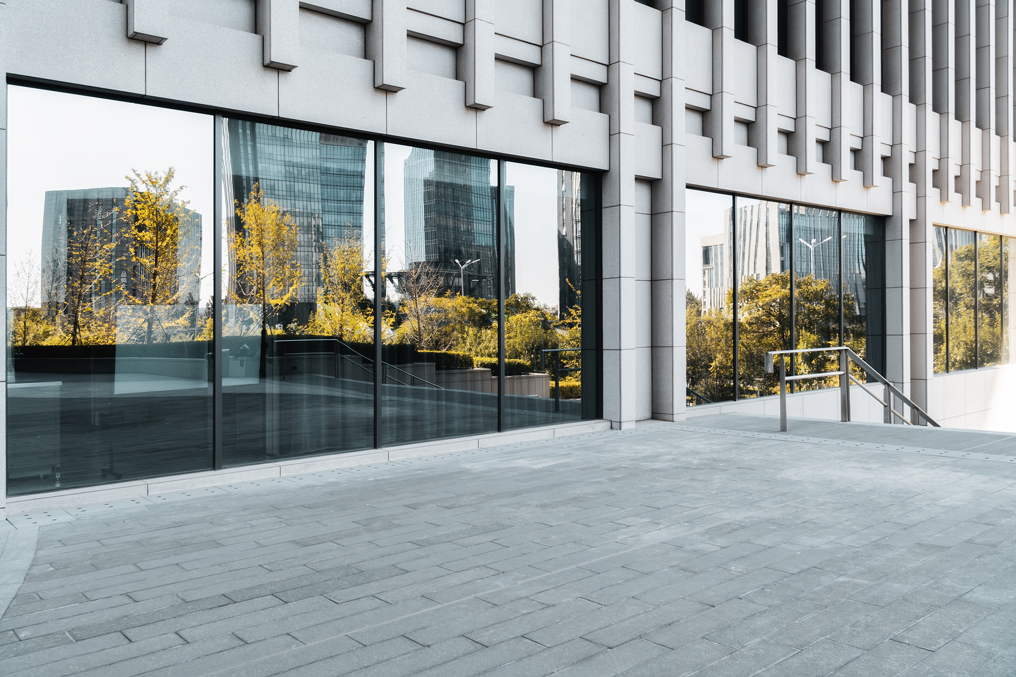 Bild av en byggnad med stora glasfönster som reflekterar träd och höga hus